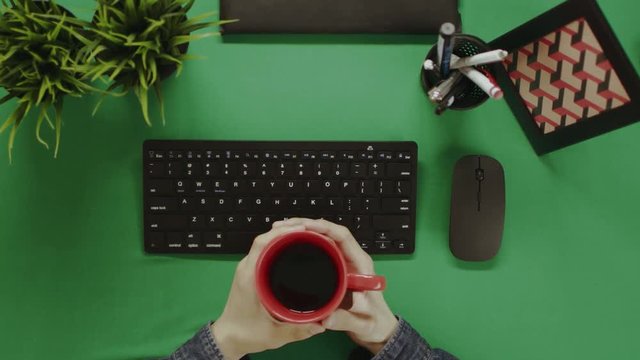 Top down shot of man sitting with cup of tea in front of computer