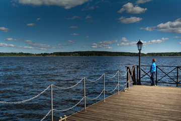 The boy stands on the edge of pier and looks into the distance.