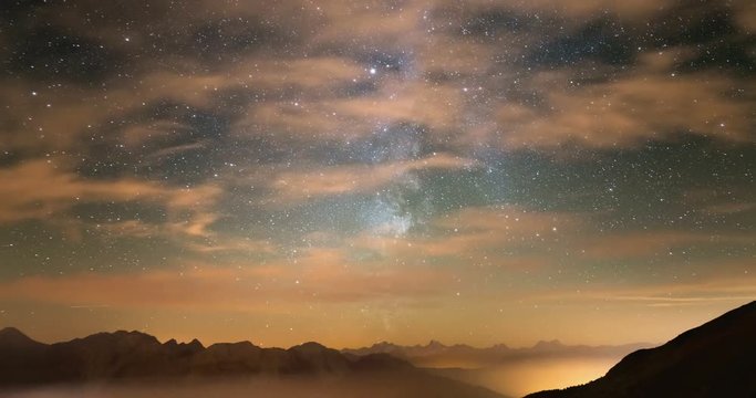 Time Lapse of the Milky way and the starry sky with clouds over the Alps and the majestic Massif des Ecrins, France. Bardonecchia Valley illuminated in the fog, Italy.
