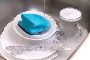dirty dishware and utensils in kitchen sink with soap foam under running water