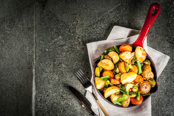 Skillet with  fried seasonal autumn vegetables (zucchini, potatoes, carrots, beans), on black stone table copy space top view