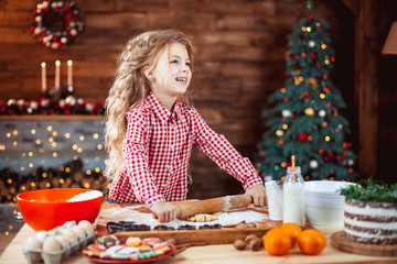 Happy little child, cute kid girl at the table in domestic kitchen making gingerbread xmas cookies decorated for Christmas holiday. Girl helping and having fun