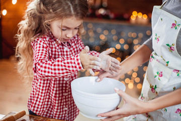 Merry Christmas and Happy Holidays. Family preparation holiday food. Mother and daughter cooking cookies in New Year interior with Christmas tree.