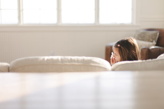 Sick Young Girl Sitting On Couch Blowing Her Nose