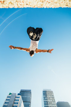 Nadir photography of a man doing a backflip in the air during a parkour training in a city