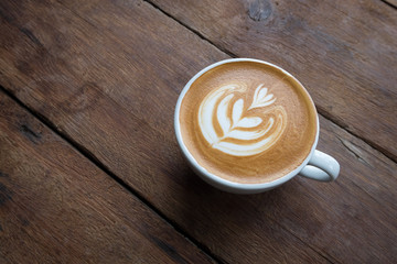 A white cup of hot latte art coffee on the wooden table in coffee shop