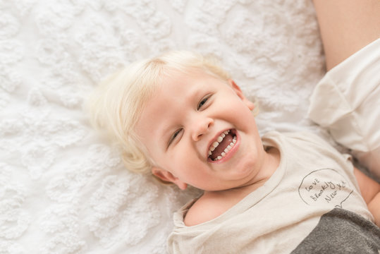 Little Boy Smiling On Bed Looking Up At Camera