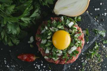 Fototapeta na wymiar Tartare steak. Beef raw chopped meat with spices, herbs and egg yolk. Fresh, spicy, delicious, gourmet meal on dark background with copy space, close-up. Top view.