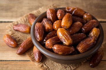 Dried dates fruit in ceramic bowl on wooden table.