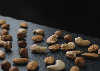 Variety of mixed nuts - almond, hazelnuts and cashew - on the dark slate background with copy space. Top view. Toned