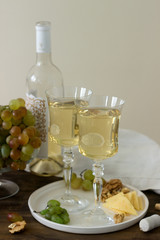 Glasses with white wine and a bottle of wine with a snack - cheese, walnuts and grapes. Rustic style.