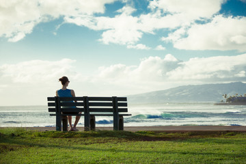 Naklejka na ściany i meble Woman relaxing on a beach park bench. 