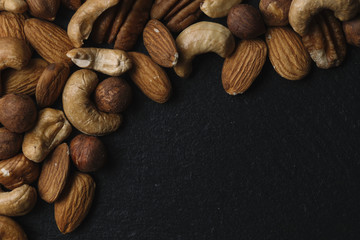 Variety of mixed nuts - almond, hazelnuts and cashew - on the dark slate background with copy space. Top view. Toned