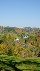 Fototapeta na wymiar Erzgebirge im Herbst/Kleines Dorf im Erzgebirge, hügelige Herbstlandschaft mit bunten Wäldern und versteckten Häusern.