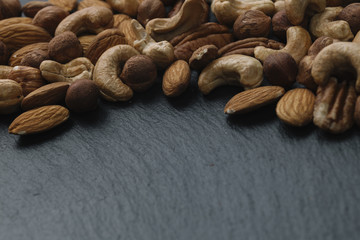 Variety of mixed nuts - almond, hazelnuts and cashew - on the dark slate background with copy space. Top view. Toned