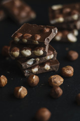 Chocolate bar pieces and nuts on dark slate background with copy space. Chocolate background. Top view. Toned