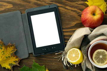 eBook and a cup of hot tea with a lemon wrapped in a scarf on a wooden table