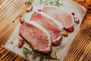 Raw pork steak on a dark wooden table with rosemary and garlic