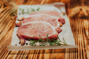 Raw pork steak on a dark wooden table with rosemary and garlic