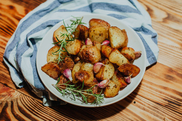 Roasted potato in white plate on wooden background with rosemary and garlic