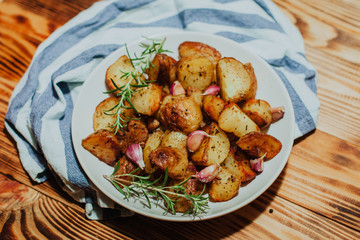 Roasted potato in white plate on wooden background with rosemary and garlic