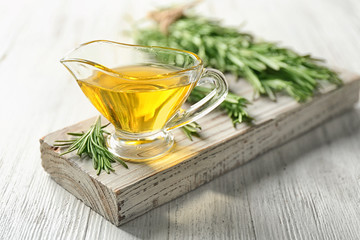 Gravy boat with rosemary oil and herb on wooden board