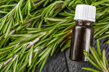 Bottle with rosemary oil and herb on wooden table