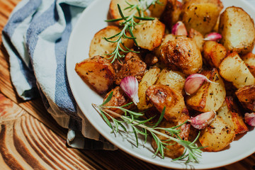 Roasted potato in white plate on wooden background with rosemary and garlic