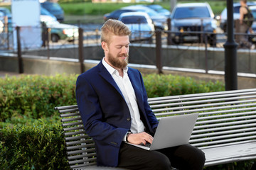 Handsome young man with laptop on bench, outdoors