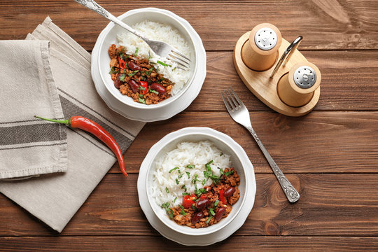 Chili con carne served with rice in bowls on wooden table