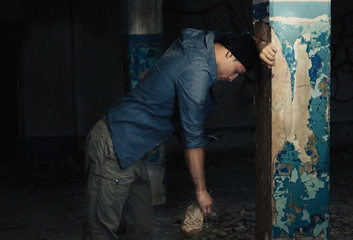 Hopeless man with bottle of alcohol in abandoned building