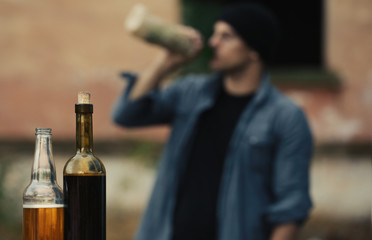 Bottles with alcohol on blurred view of drunk man