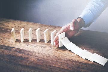 Businessman stopping wooden dominoes bricks from crumbling with his hand.