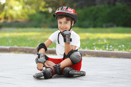 Cute boy on roller skates sitting in park