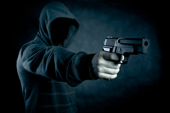Hooded man with a gun in the dark 