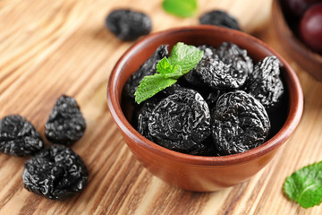 Bowl with tasty dried plums on table