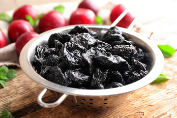 Collander with tasty dried plums on table