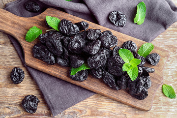 Board with tasty dried plums on table