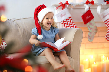 Obraz premium Cute little girl in Christmas hat reading book at home