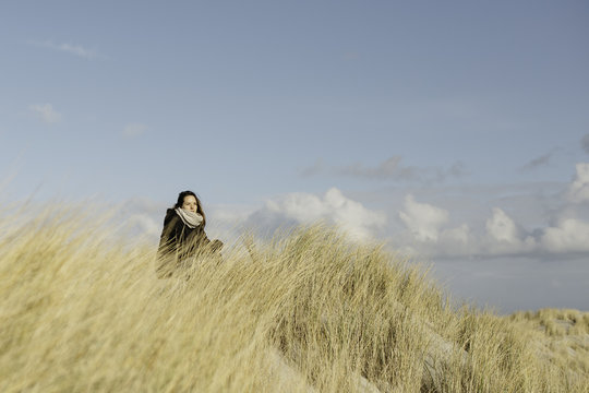 Young woman sits in between dune grass in the dunes.