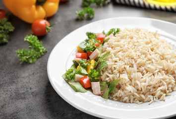 Plate with delicious brown rice and vegetables on table