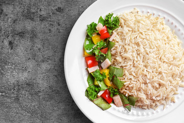 Plate with delicious brown rice and vegetables on table