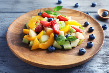 Plate with delicious fruit salad on wooden background