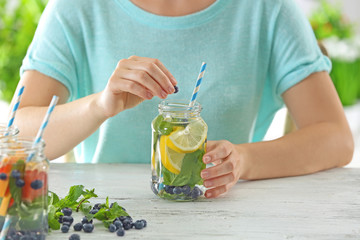 Young woman drinking infused water with fruits at wooden table