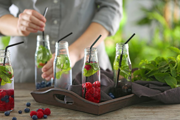 Bottles of healthy infused water and blurred woman on background