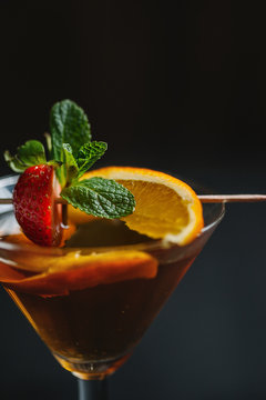 Detail side shot of a cocktail garnished with strawberry,mint and orange.