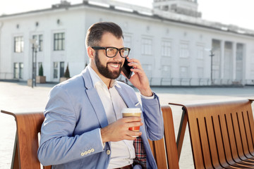 Handsome successful businessman talking on mobile phone while drinking coffee outdoors