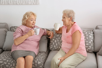 Elderly women drinking coffee while sitting on sofa at home