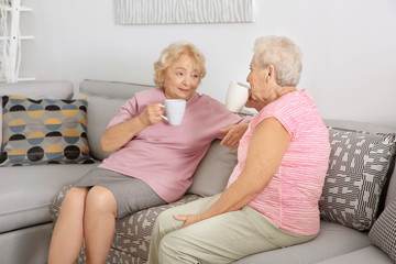 Elderly women drinking coffee while sitting on sofa at home