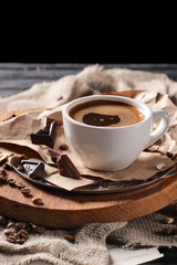 Composition with cup of coffee and served with coffee beans and chocolate on wooden chopping board over black background